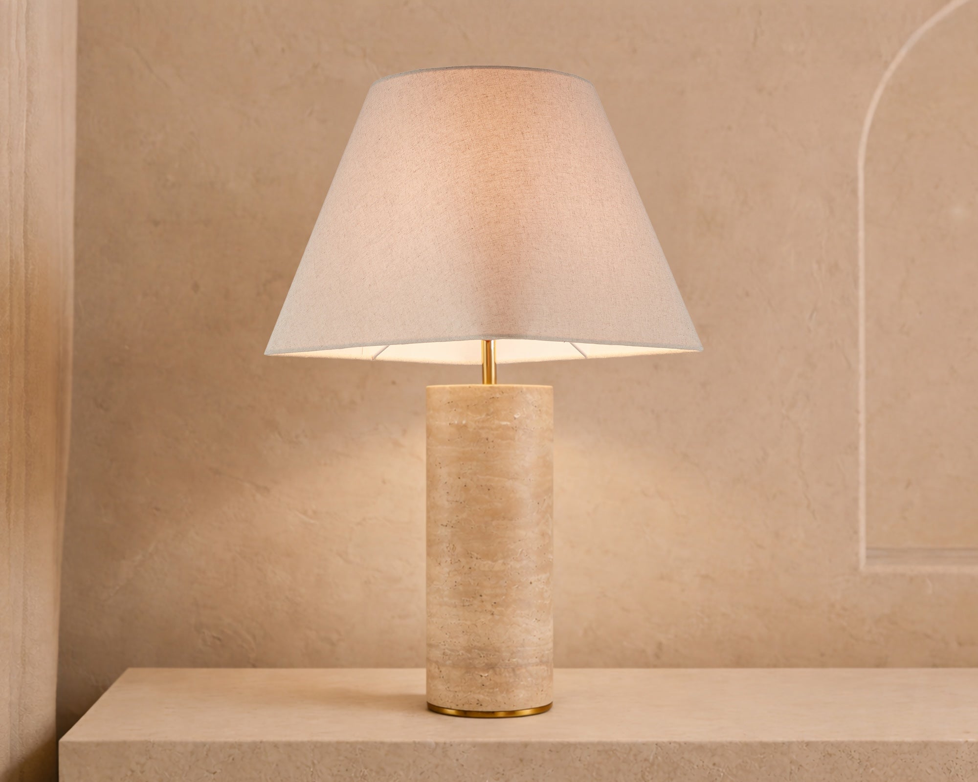 Corina Table Lamp by Liang & Eimil featuring a travertine marble cylindrical base with antique brass detailing and a beige linen shade